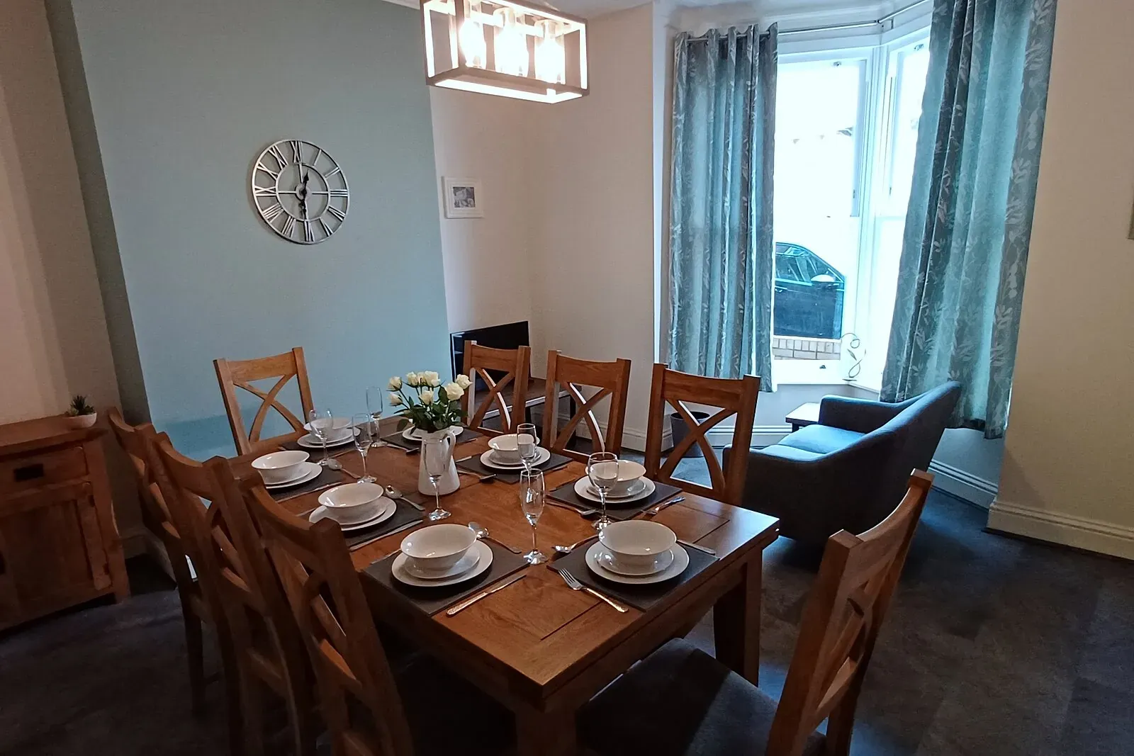 Oak dining table laid for eight beneath a pendant light in the bay-windowed dining room